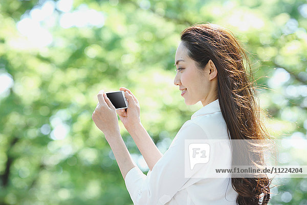 Young Japanese woman with smartphone surrounded by green in a city park