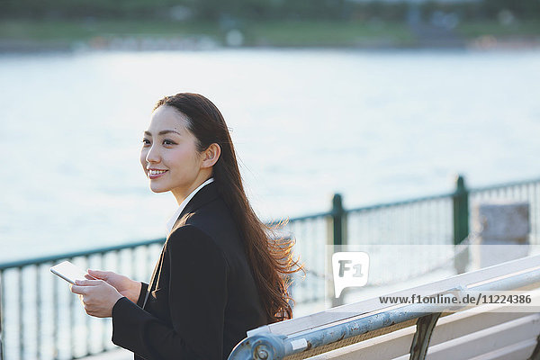 Junge japanische Geschäftsfrau mit Tablet an einem Fluss in der Innenstadt von Tokio