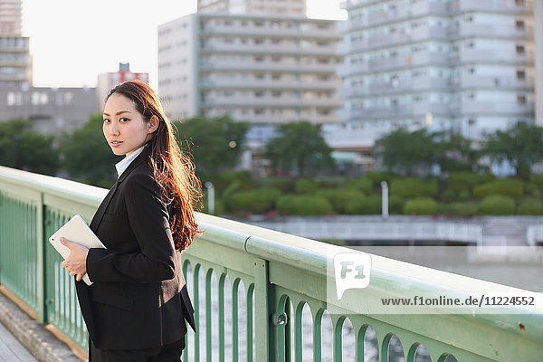 Porträt einer jungen japanischen Geschäftsfrau an einem Fluss in der Innenstadt von Tokio