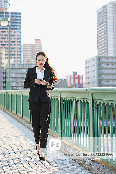 Junge japanische Geschäftsfrau mit Smartphone an einem Fluss in der Innenstadt von Tokio