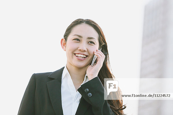 Junge japanische Geschäftsfrau am Telefon an einem Fluss in der Innenstadt von Tokio