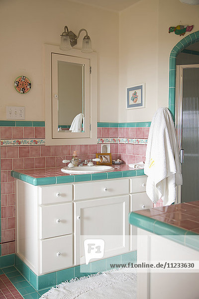 Waschbecken und Tresen in einem rosa und blaugrün gefliesten Badezimmer
