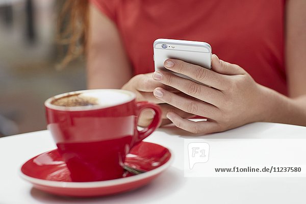 Frau benutzt Smartphone mit Kaffee