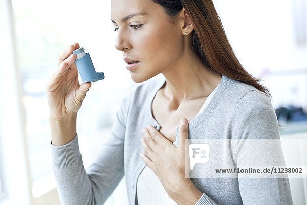 Junge Frau benutzt Inhalator und berührt die Brust