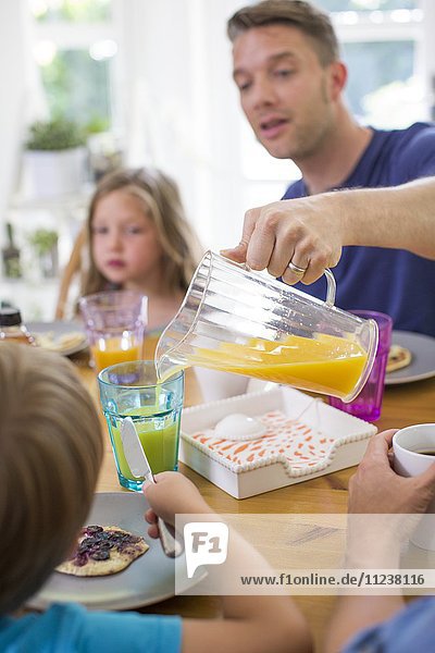 Father pouring orange juice at breakfast