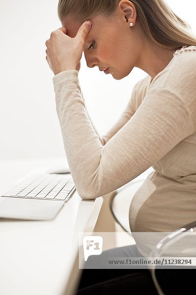Pregnant woman at desk with head in hands