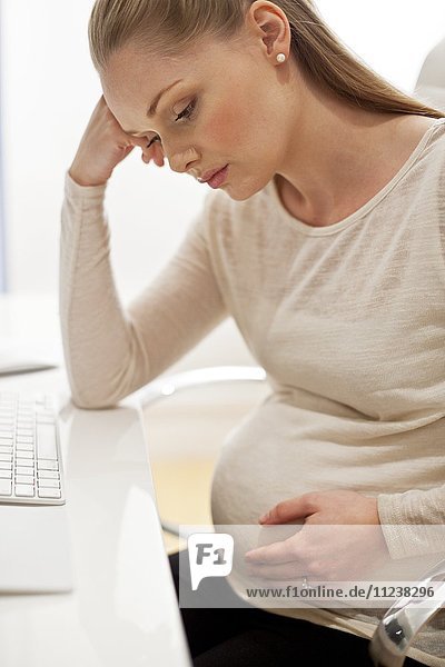 Schwangere Frau am Schreibtisch mit Kopf in den Händen
