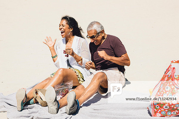 Senior couple sitting on picnic blanket on beach  laughing  Long Beach  California  USA