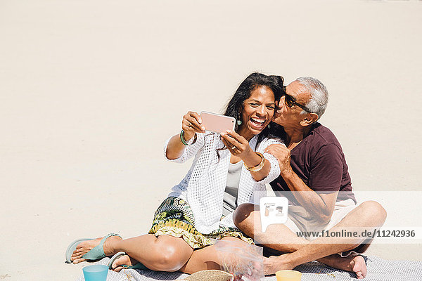 Senior couple sitting on beach  taking selfie with smartphone  Long Beach  California  USA