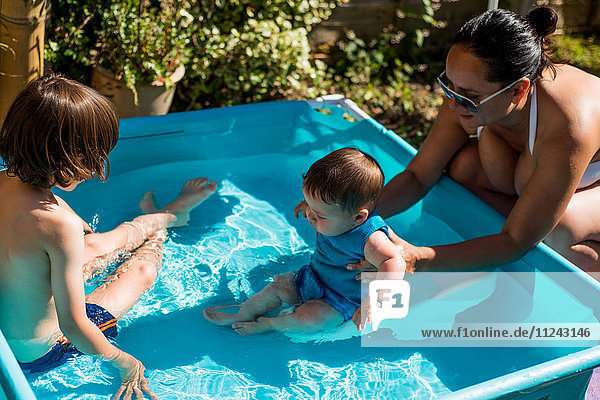 Mutter und Söhne spielen am Sommertag im aufblasbaren Schwimmbad