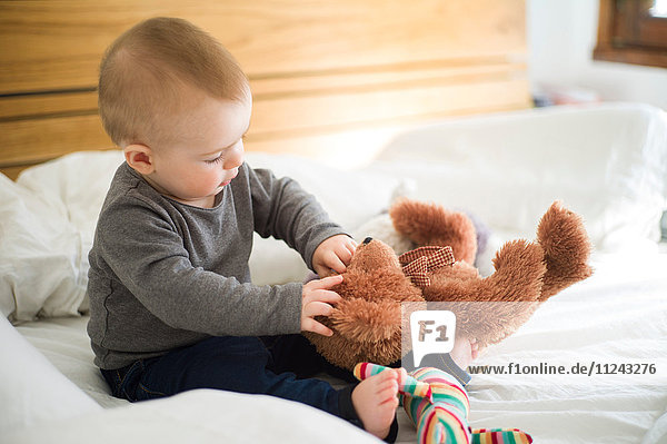 Kleines Mädchen sitzt auf dem Bett und spielt mit Teddybär