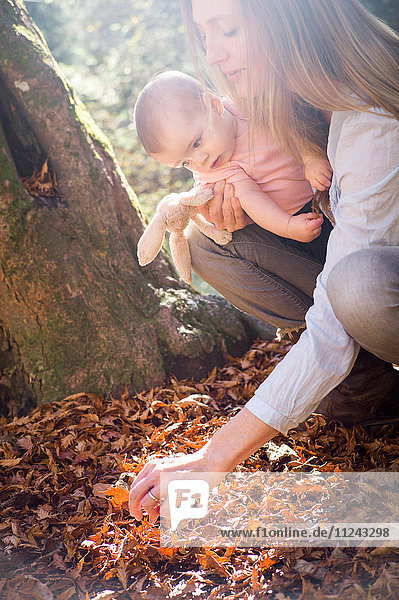 Mutter und Tochter kauern und untersuchen Blätter auf dem Waldboden