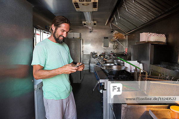 Mann im Fastfood-Wohnwagen  schaut auf Smartphone und lächelt