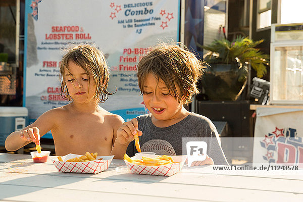 Zwei kleine Jungen essen Fastfood neben einem Fastfood-Anhänger