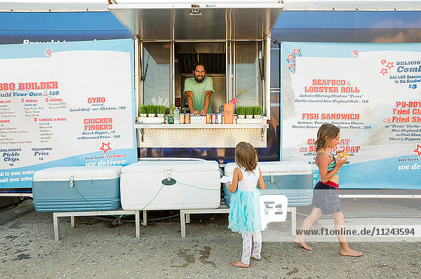Mann in Fast-Food-Wohnwagen serviert zwei junge Mädchen neben einem Wohnwagen