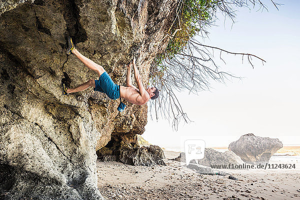 Male free climber climbing rock overhang on Pandawa Beach Bali Indonesia