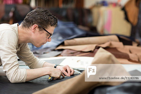 Mann schneidet Leder mit Gebrauchsmesser in Lederjackenherstellern