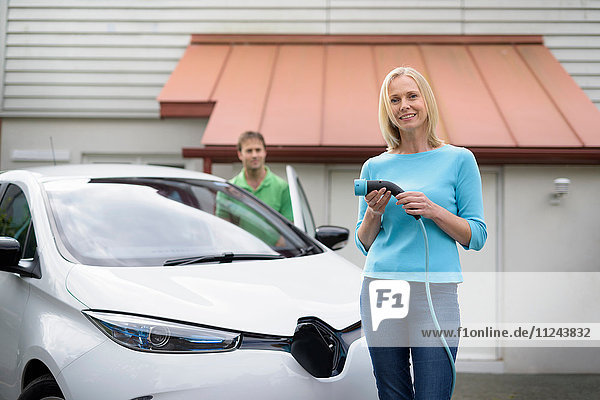 Porträt einer Frau mit Elektroauto Ladestecker haltend