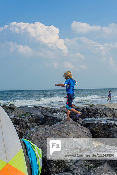 Junge klettert am Meer auf Felsen  Rückansicht