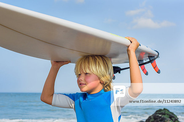 Young boy at beach  carrying surfboard on head