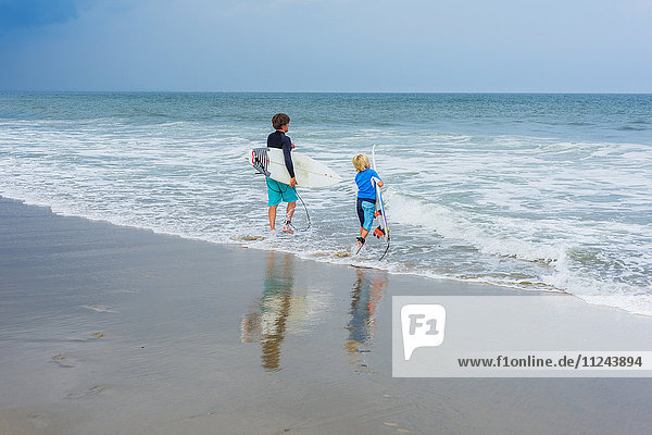Father and son standing in sea  holding surfboards  rear view