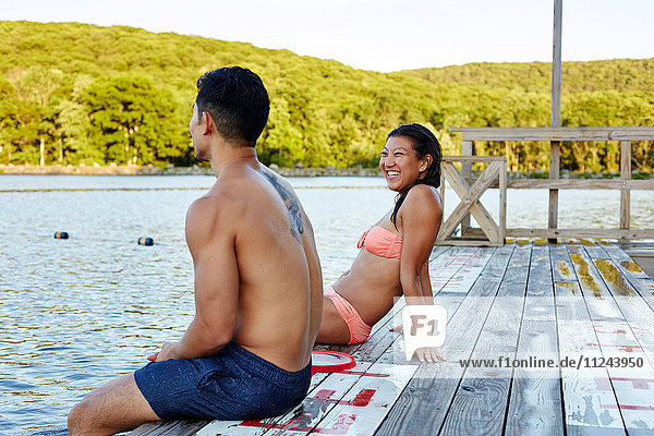 Junges Paar auf dem Pier am See sitzend  Rückansicht