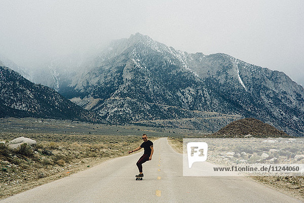 Mann fährt Skateboard auf der Strasse durch die Berge  Lone Pine  Kalifornien  USA