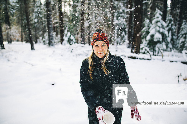 Woman in snow-covered forest throwing snow from cup