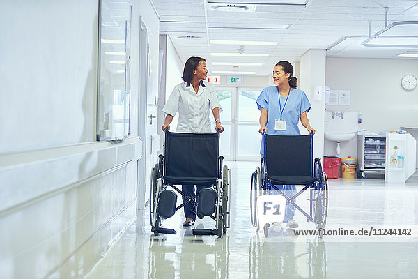 Female orderlies pushing wheelchairs along hospital corridor