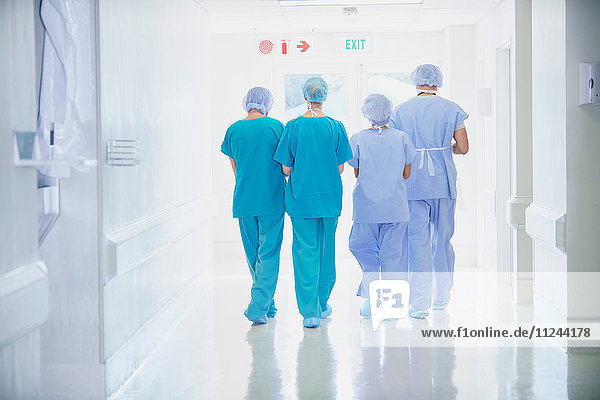Rear view of four medical staff wearing scrubs walking in hospital corridor