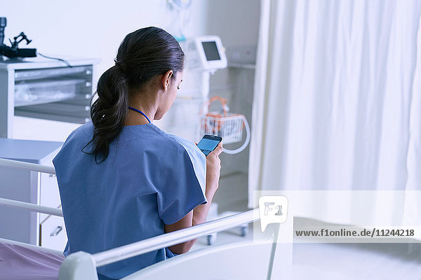 Female medic sitting on hospital bed reading smartphone texts