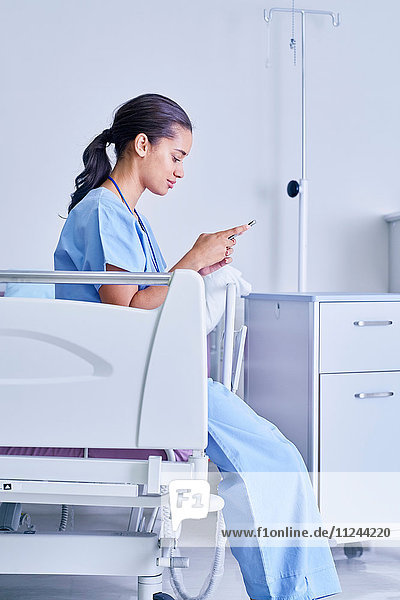 Female medic sitting on hospital bed reading smartphone text messages