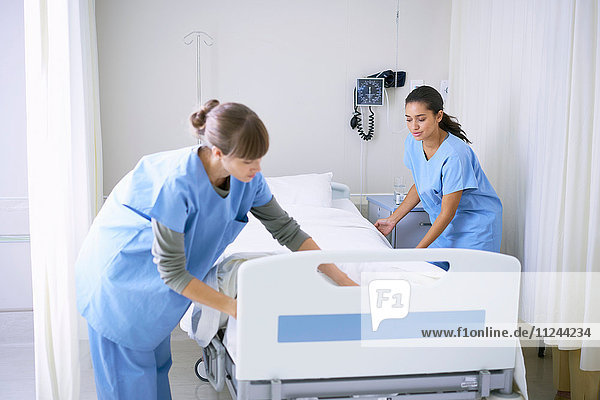Two female nurses making hospital bed in ward