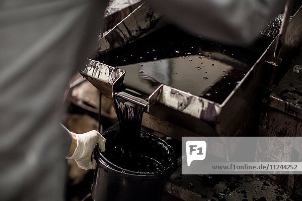 Cropped view of mid adult man pouring tar into bucket