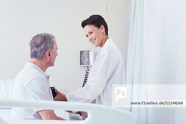 Female doctor using blood pressure gauge on senior male patient on hospital bed