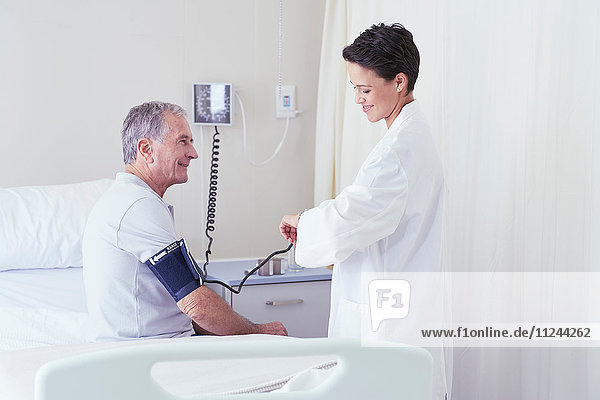 Female doctor using blood pressure gauge and timing pulse of senior male patient
