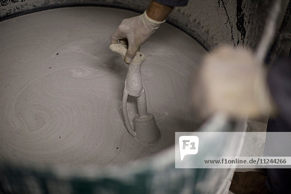 Artist dipping object into vat of plaster of paris