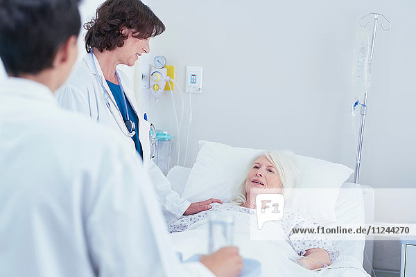 Doctors explaining to senior female patient in hospital bed