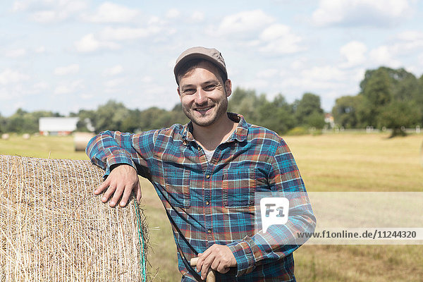 Farmer leaning against hay bale looking at camera smiling