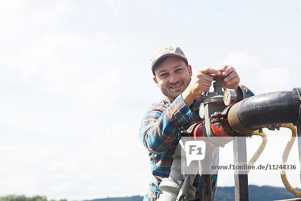 Mann öffnet Ventil an Industrierohrleitungen und schaut lächelnd in die Kamera