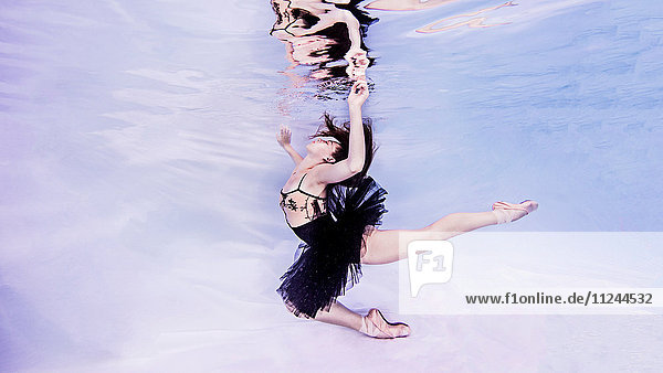 Unterwasseraufnahme einer Frau in Tutu- und Ballettschuhen Hand bricht Wasseroberfläche