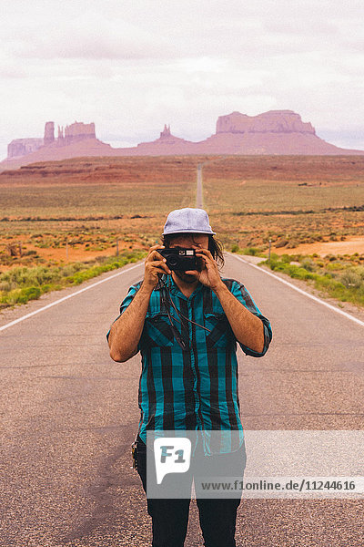 Young man taking photographs from road Monument Valley Arizona USA