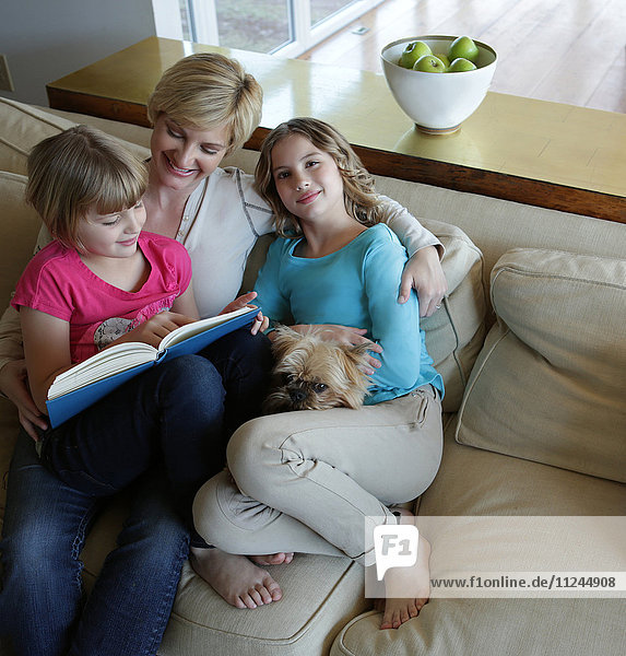 Mutter und Töchter auf Sofa sitzend mit Hund  Lesebuch