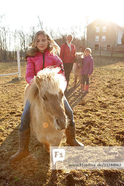Junges Mädchen reitet Pony  Mutter und Schwester schauen von hinten zu