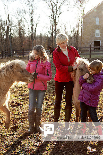 Mutter und zwei Töchter  im Freien  stehend mit Ponys