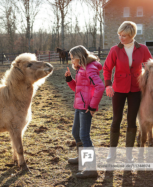 Mutter und Tochter im Freien  Tochter gibt Anweisungen an Pony