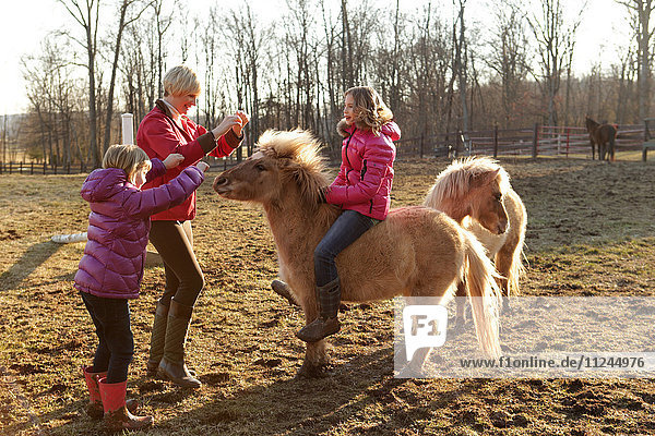 Junges Mädchen auf Pony reitend  Mutter und Schwester neben ihnen stehend