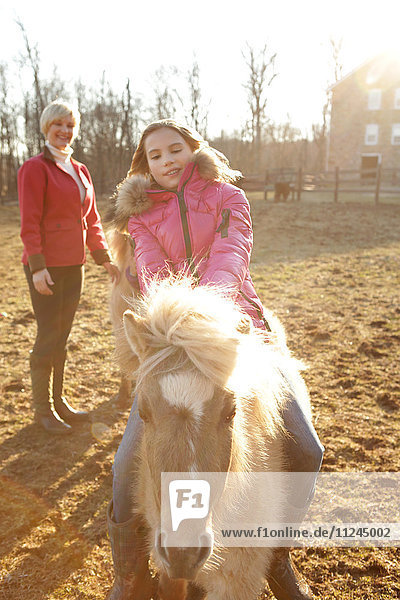 Junges Mädchen reitet Pony  Mutter schaut von hinten zu