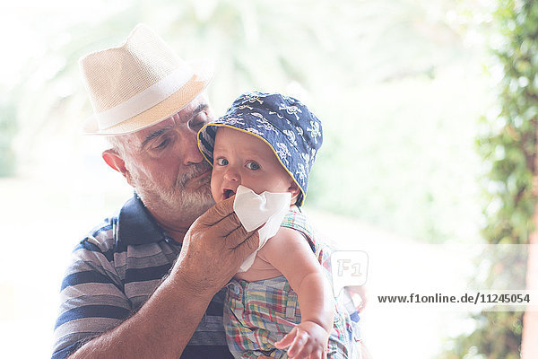 Grossvater wischt dem Baby das Kinn mit einem Taschentuch ab