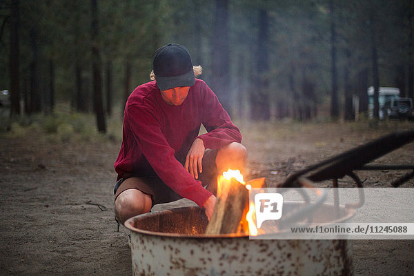 Young man crouching at camp bonfire in forest at dusk  Mammoth Lakes  California  USA